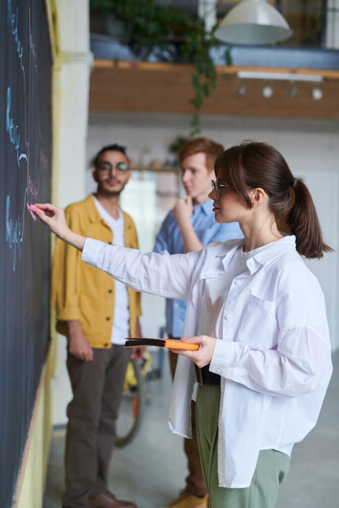 pexels-photo-3184644-3184644 A group of young people discussing ideas at a blackboard in a modern office setting.